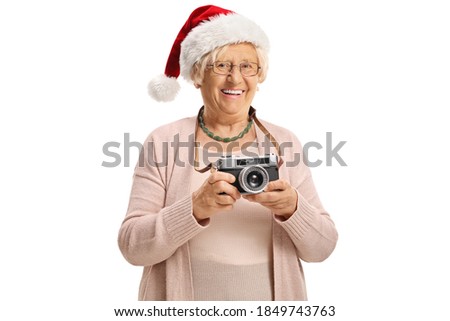Elderly lady wearing a santa claus hat and holding a vintage camera isolated on white background