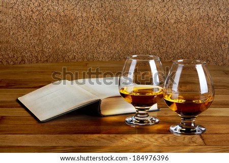 Two goblets of brandy and open book on wooden old counter top