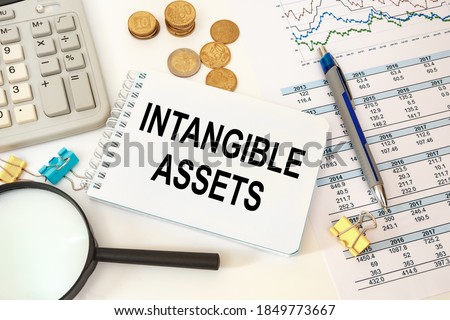 Intangible assets is written on a notepad on an office desk with office accessories. Royalty-Free Stock Photo #1849773667