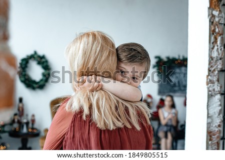 Mom blonde holds her son in her arms. Love and care concept. The child hugs mom. Christmas decorations in the background. Royalty-Free Stock Photo #1849805515