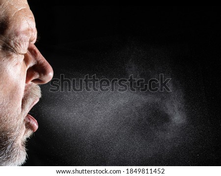 A man sprays aerosols into the air while speaking. The background is black. Royalty-Free Stock Photo #1849811452