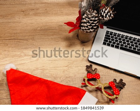 View from above on wooden table on which there is laptop and red Santa Claus hat, Christmas decorations: funny glasses, Christmas tree with bumps. online connection from home. celebration via Internet