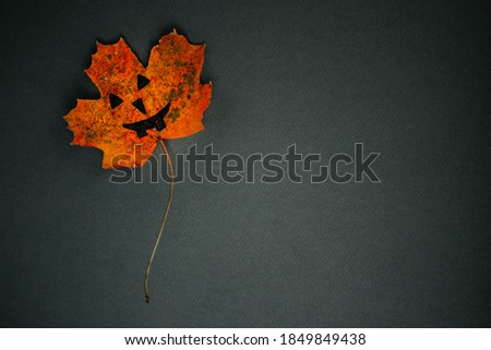 Maple leaf with painted face as decoration for Halloween holiday. Creative concept. Copy space.