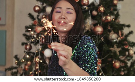 A woman lights sparklers against the background of a Christmas tree decorated for the holiday. Celebrating winter holidays