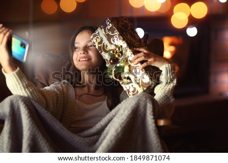 young girl takes a picture of herself with a phone with a Christmas present