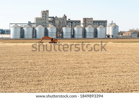 The excavator stands against the background silver silos. Agro manufacturing plant for processing drying, cleaning and storage of agricultural products. Large iron barrels. Granary elevator