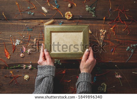 Female hands holds photo frame next to dry herbs on wooden table 