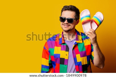 style guy in 90s shirt and pixel sunglasses holds flip flops on yellow background