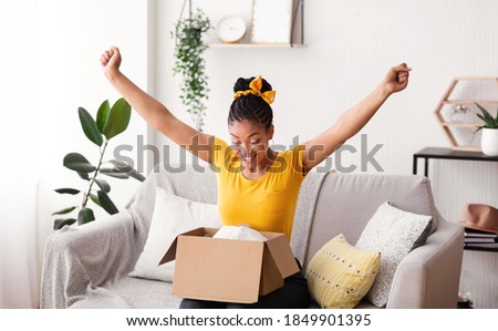 Excited african american woman received parcel, opening cardboard box at home, satisfied with great purchase, happy female model unpacking package looking inside overjoyed by postal shipping delivery Royalty-Free Stock Photo #1849901395