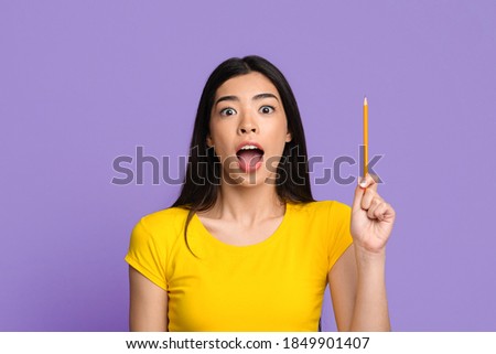 Excited Asian Lady Raising Pencil Up, Having Idea Or Got An Inspiration, Young Smart Korean Woman Standing Over Purple Background In Studio And Looking At Camera, Exclaiming Eureka, Copy Space
