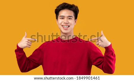 Choose An Pick Me. Self-assured and charismatic asian man pointing at self, wearing red sweater. Egocentric man promoting himself, indicating his body, isolated over orange studio background