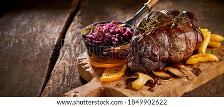 Gourmet German venison roast with red cabbage, mushrooms, orange and potato chips served on a wooden board in a panorama banner Royalty-Free Stock Photo #1849902622
