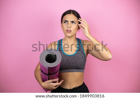 Young beautiful woman wearing sportswear over isolated pink background confuse and wonder about question. Uncertain with doubt, thinking with hand on head. Holding a splinter in her hand.