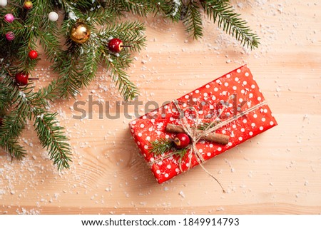 Festive gift box, decorated with red dotted paper, twine, cinnamon stick and fir-tree branch. Christmas decoration in the corner of the picture, festive mood.