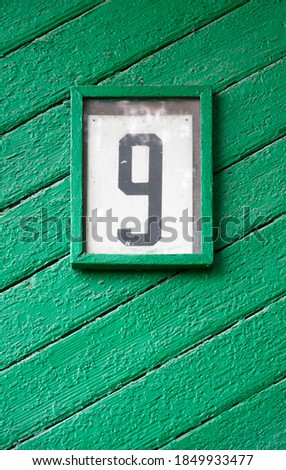 House number plate (number nine) on the green wall of a wooden old building