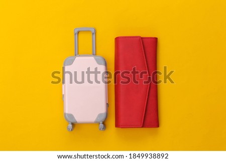 Travel flat lay. Mini plastic travel suitcase, red wallet on yellow background. Minimal style. Top view