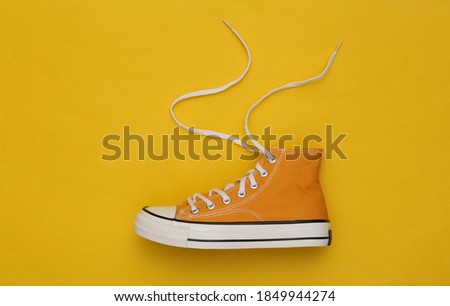 Yellow high-top sneaker (gumshoe) with untied laces on a yellow background. Top view. Minimalism