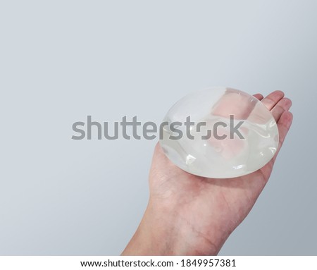 Silicone breast implant surgery gel type and smooth skin touch surface in hand on gray background, medical equipment.