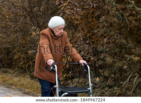 Elderly woman taking a walk in autumn with walker aid to enjoy fresh air
