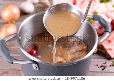Saucepan with bouillon with a ladle on the table. Bone broth Royalty-Free Stock Photo #1849971106