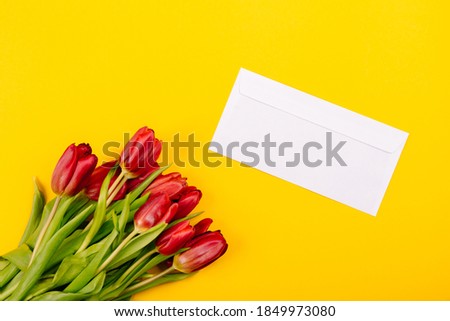 White gift envelope on a yellow background with a bouquet of red tulips and a free place for text. Sample certificate or invitation card. Close-up.