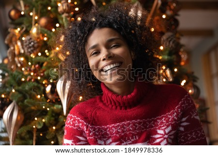 Head shot portrait overjoyed African American woman laughing, looking at camera, posing on Christmas tree background at home, blogger shooting vlog, having fun, using webcam, making video call