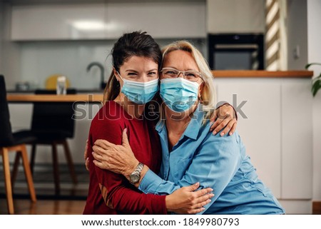 Mother and daughter with protective surgical face masks on sitting on the floor and hugging during corona virus outbreak. Even it is corona outbreak we still can share love. Royalty-Free Stock Photo #1849980793