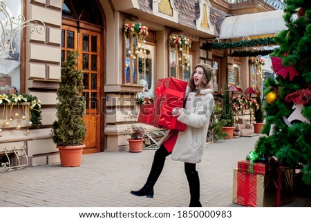 Portrait Happy good-looking woman is holding gift box in her hands and smiling while standing outdoors. Beautiful happy girl posing with Christmas presents. New Year preparation