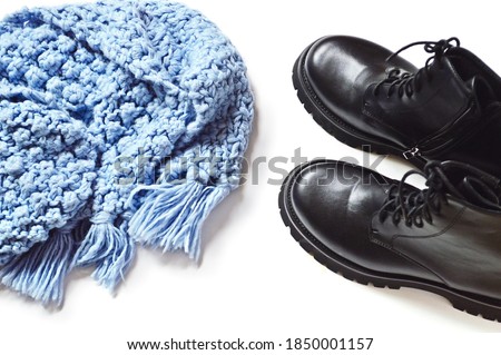 Blue knitted scarf and black ankle boots on a white. Flat lay fashion photography. Winter season trends, january sale