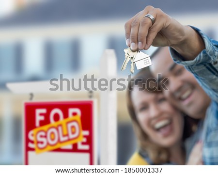 Mixed Race Couple in Front of Sold Real Estate Sign and House with Keys.