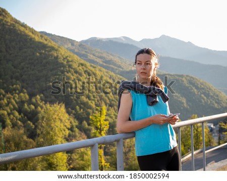 young female athlete on a morning jog uses a mobile app to track her results. Portrait of a sunrise in the mountains