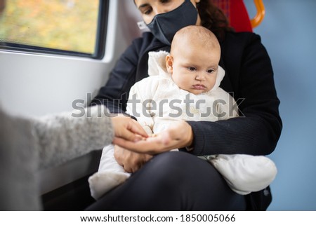 Arm of a little girl in a gray sweater taking pistachios from the hand of her mother who's holding baby sister