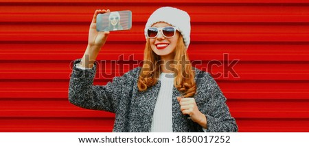 Portrait of happy smiling young woman taking selfie picture by phone over red background