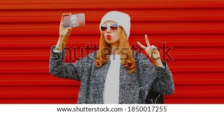 young woman taking selfie picture by phone over red background