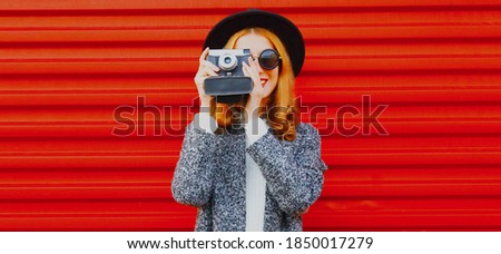 young woman photographer with vintage film camera wearing a black round hat over red background