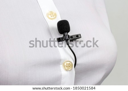 Audio recording of sound on a condenser microphone. The lavalier microphone is secured with a clip on a woman's shirt close-up.