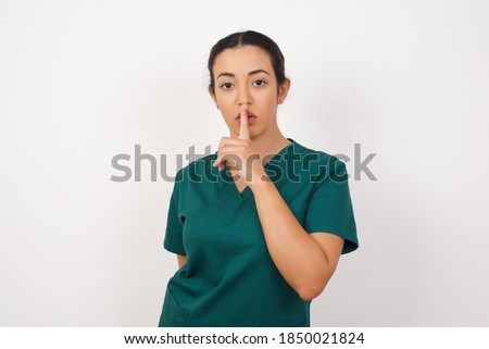 Young arab doctor surgeon woman over isolated white background makes silence gesture, keeps finger over lips. Silence and secret concept.