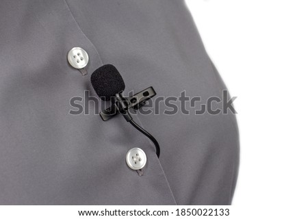 The lavalier microphone is secured with a clip on a gray women's shirt close-up. Audio recording of the sound of the voice on a condenser microphone.
