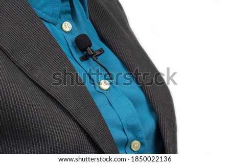 The lavalier microphone is secured with a clip on a blue women's shirt close-up. Audio recording of the sound of the voice on a condenser microphone.
