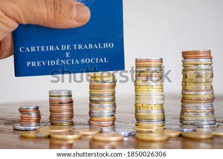 Brazilian Work Card with stacks of coins on the table. Job and economy concept. Portuguese text "Labor and Social Security Card". Minimum wage increase (Aumento do salário mínimo)
