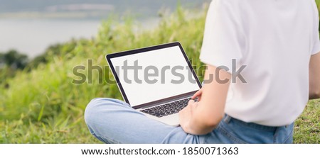 Woman sitting on the grass floor and using laptop screen is blank are with beautiful nature on a bright day.