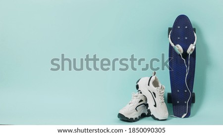 White sneakers, blue skateboard and white headphones on a blue background. Sports style. Place for text.