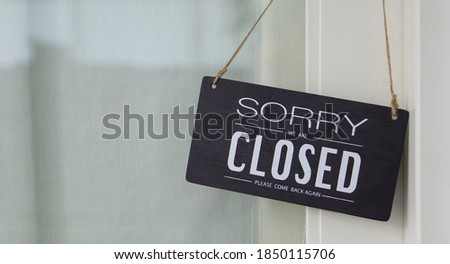 A "CLOSED" wooden sign hanging on the glass door in front of the coffee shop.