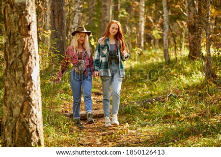 two friendly women hiking together, go forward in the forest. young and beautiful travellers in the nature