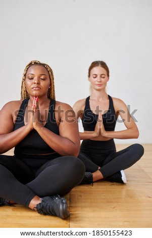 calm afro american and caucasian women in sportswear meditating, keep calm sitting on the floor, sit with eyes closed