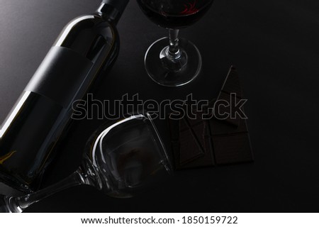Elegant bottle and wineglasses of red wine with dark chocolate on black background. Top view. Concept of advertising and promotion of alcoholic drinks. Space for text. Flat lay.