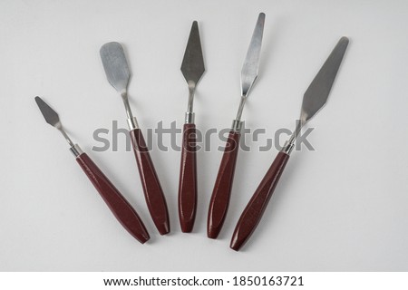 Five art palette knives lie on a white art canvas. Royalty-Free Stock Photo #1850163721