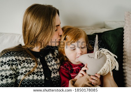 Little baby girl and mom having fun and play toys on bed at home. Childhood concept. Merry Christmas and Happy Holidays.