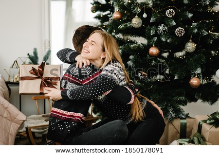 Man exchanging gifts with woman near tree. Young couple hugging in love. Couple celebrating Christmas together at home. Merry Christmas and Happy Holidays. Happy New Year 2021.