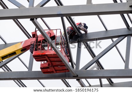 Man worker on a crane performs high-rise work on welding metal structures of a new tower at a height.